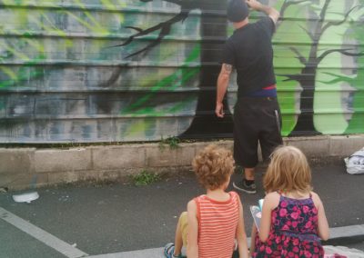 Rêve de verdure et nature ! Des enfants assis rue de la Paix dessinent, sur le trottoir, devant les taules ondulées, et la mise en oeuvre de street art, avant les travaux de renaturation par l'association Agiv et la pause de grilles...